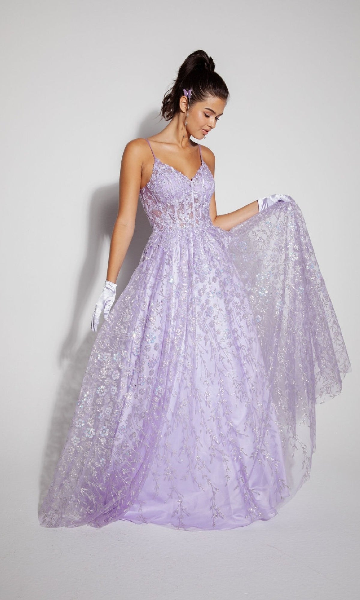 A woman wearing the Long Glitter A-Line Prom Dress: Eureka 9908, featuring lilac floral embroidery, stands against a plain background, holding out part of her dress while accessorizing with white gloves and a matching hairpiece.